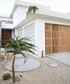 a white house with wooden garage doors and plants in the front yard, along with graveled walkways