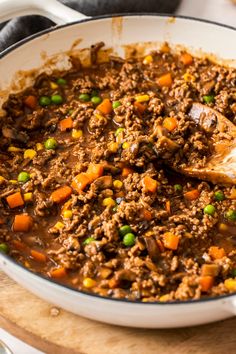 a pot filled with meat and vegetables on top of a wooden cutting board next to a spoon