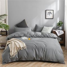 a bed with grey sheets and pillows in a room next to a potted plant