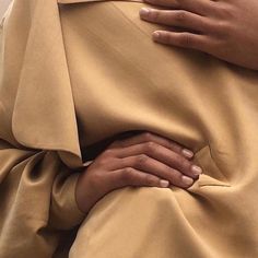 a woman with her hands on her stomach wearing a tan dress and matching ring finger