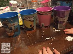 three cups with cartoon characters on them are sitting on a table next to two hands