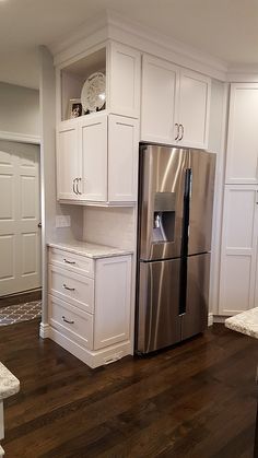 a kitchen with white cabinets and stainless steel refrigerator freezer combo in the center, along with hardwood flooring