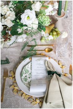 the table is set with white flowers and green napkins, gold place settings and silverware