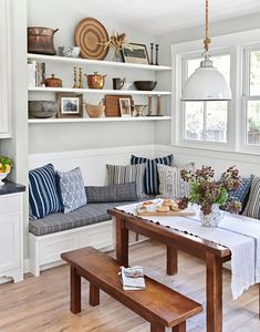 a kitchen with white walls and wooden floors, built in shelving unit above the dining room table