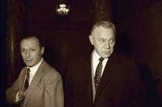 two men in suits and ties standing next to each other with one looking at the camera