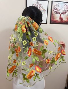 a woman wearing a sheer scarf with flowers on it, and two framed pictures behind her