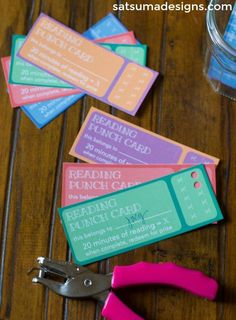 some pink scissors are sitting next to some ticket holders on a wooden table with water in the background