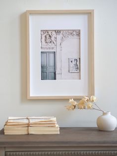 a white vase with flowers on top of a wooden table next to a framed photo