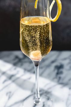 a wine glass filled with champagne and topped with lemon wedges on a marble table