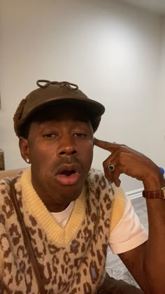 a man wearing a hat and vest sitting on a couch with his hand under his chin