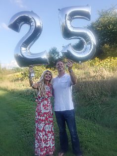 a man and woman holding up the number twenty five balloons