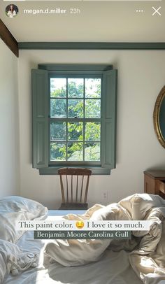 an unmade bed sitting under a window next to a wooden table with a mirror on it