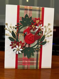 a red bird sitting on top of a card with flowers and leaves in it's beak