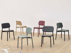 six chairs in different colors and sizes on a wooden floor with white wall behind them