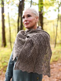 a woman standing in the woods wearing a shawl