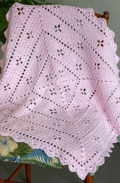 a pink crocheted blanket sitting on top of a chair next to a potted plant