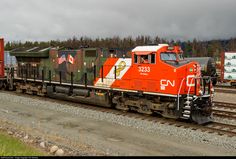 an orange and white train engine pulling its cars down the tracks in front of some trees