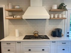 a stove top oven sitting inside of a kitchen next to white cabinets and open shelves