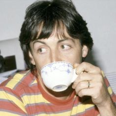 a man drinking from a coffee cup while sitting on a bed with his eyes wide open