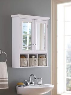 a white sink sitting under a bathroom mirror next to a wall mounted cabinet with baskets on it