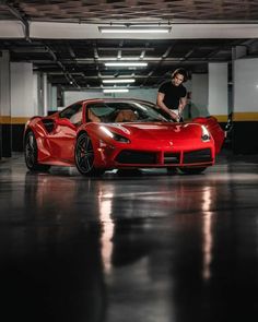 a man standing next to a red sports car in a parking garage with his hand on the door handle