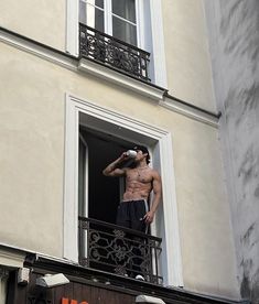 a shirtless man drinking from a bottle on top of a balcony next to a building