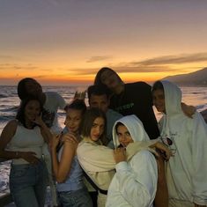 a group of young people standing next to each other near the ocean at sunset or sunrise