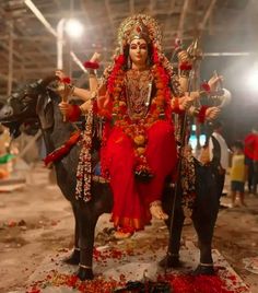 a statue of a woman sitting on top of an elephant in a building with flowers all over the floor