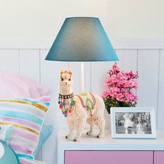 a llama figurine on a nightstand next to a blue lamp and pink flowers