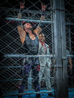 two men in wrestling gear standing behind a cage with their hands up to the sky