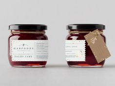 two jars of jam sitting next to each other on a white surface with a brown tag