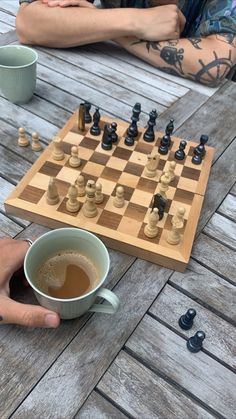 a person sitting at a table with a chess board and cup of coffee in front of them