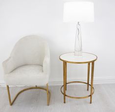 a white chair next to a table with a lamp on it and a glass vase