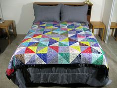 a bed with a colorful quilt on top of it and two night stands next to it