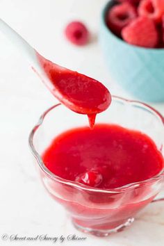 a spoon full of raspberry sauce in a glass bowl with fresh raspberries