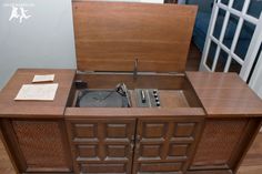 an old fashioned record player in a wooden cabinet with papers on the floor next to it