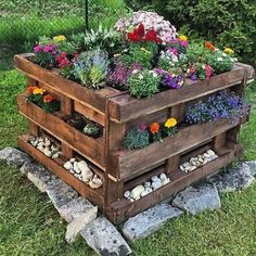 a wooden planter filled with lots of flowers on top of a grass covered field