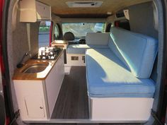 the interior of a camper van with blue couches and wood counter tops,