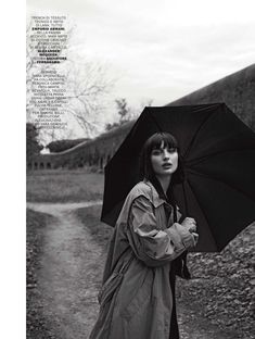 a woman holding an umbrella while standing on a dirt road next to a tree and hill