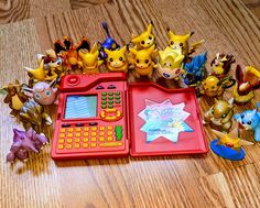 a red toy calculator surrounded by pokemon figurines on a wooden floor