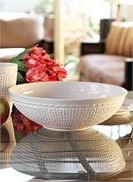 a table topped with two white bowls filled with fruit next to a vase full of flowers