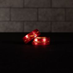 two red ribbon wrapped rings sitting on top of a black table next to a brick wall