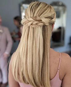 a woman with long blonde hair wearing a half - up braid and pink dress in the background