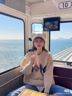 a woman sitting on top of a train next to the ocean