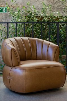 a brown leather chair sitting on top of a cement floor next to a black fence