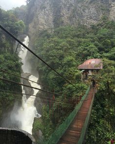 a suspension bridge over a river with a waterfall in the background