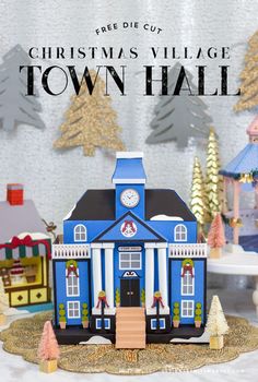 a blue and white town hall with christmas trees in the background, on a table