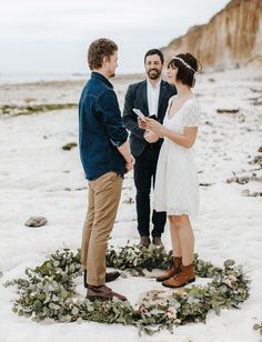 a man and woman standing in the snow during their wedding ceremony with greenery around them