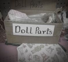 a cardboard box with doll parts in it on top of a pile of cloths