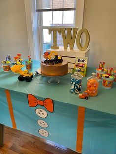 a table topped with a cake covered in frosting next to a sign that says two